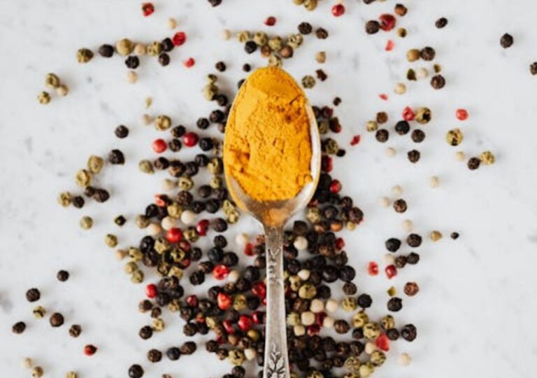 Sproszkowana kurkuma na łyżeczce i ziarna kolorowego pieprzu