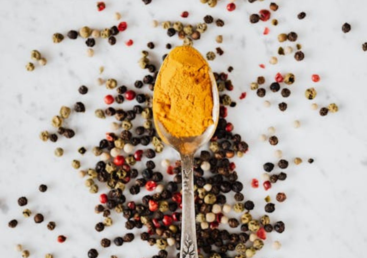 Sproszkowana kurkuma na łyżeczce i ziarna kolorowego pieprzu