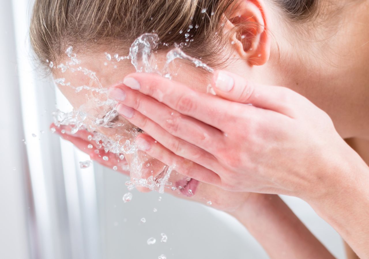 Młoda kobieta myje twarz wodą