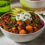Klasyczne chili con carne podane w białej misce z dodatkiem śmietany i awokado