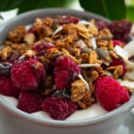 Jogurt z granolą i świeżymi malinami, podany w białej miseczce